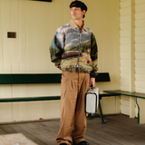 Person wearing a patterned jacket and holding a suitcase on a wooden porch.