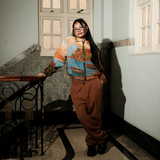 Person wearing a colorful sweater and brown pants standing in a room with a window.